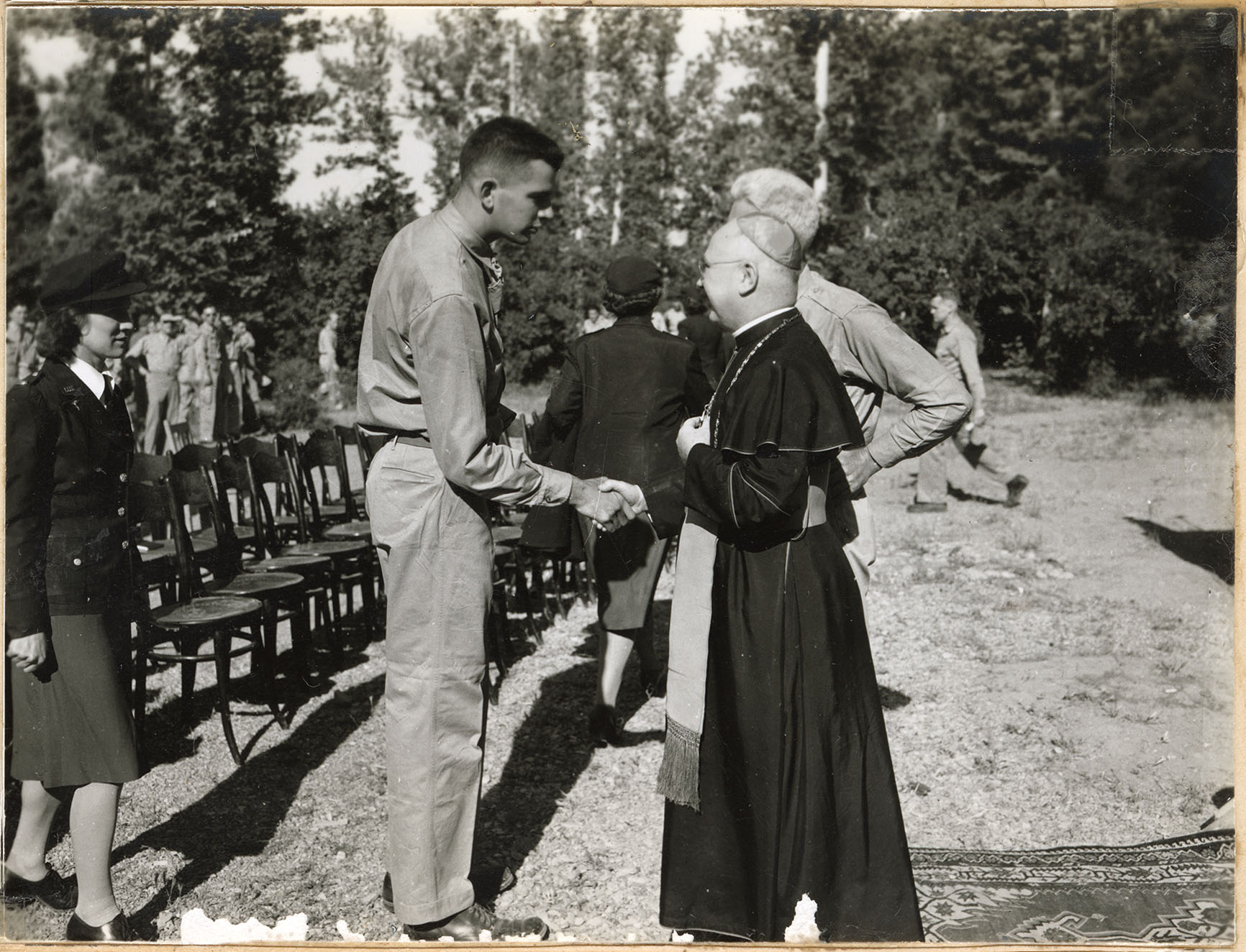 A tall soldier greets a clergyman in robes while a woman in uniform waits A tall soldier greets a clergyman in robes while a woman in uniform waits